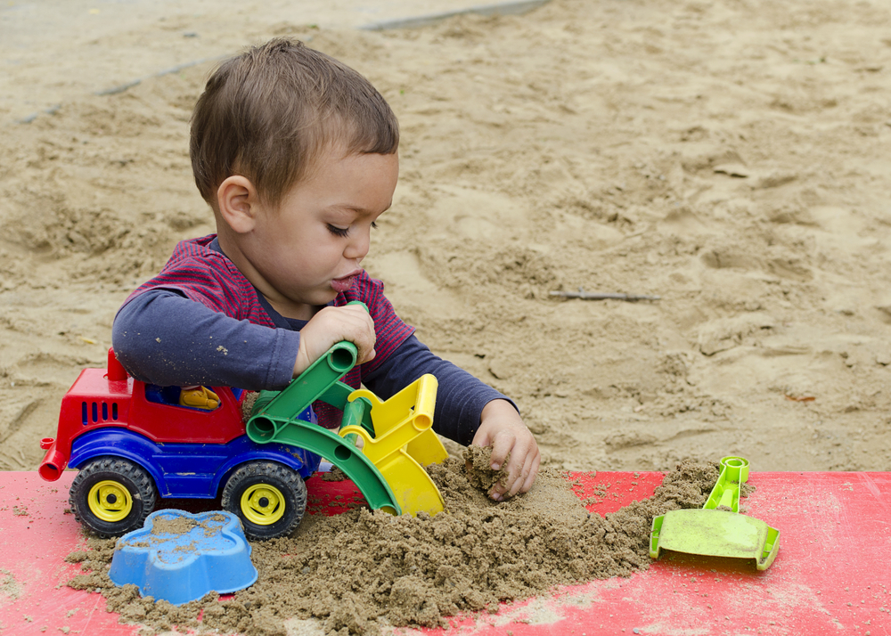 Child playing in a sandpit with a toy digger