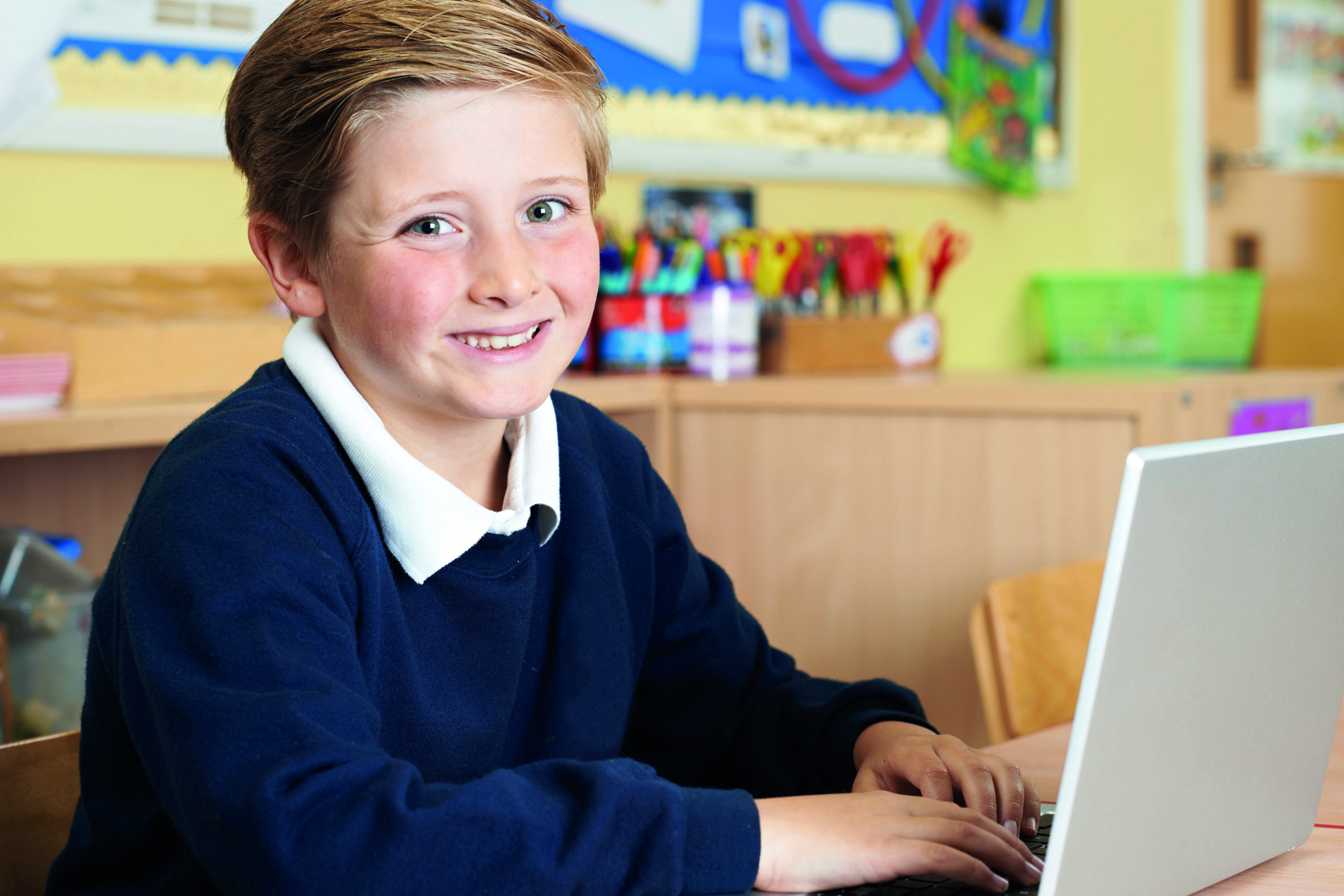 Young child smiling whilst sat in front of a laptop