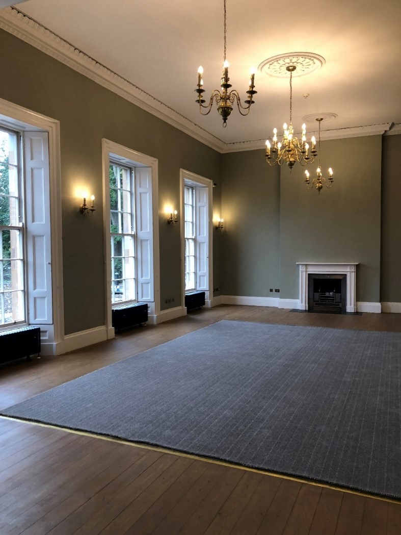 Interior view of a one of the grand rooms with period features, dark green walls and and three chandeliers