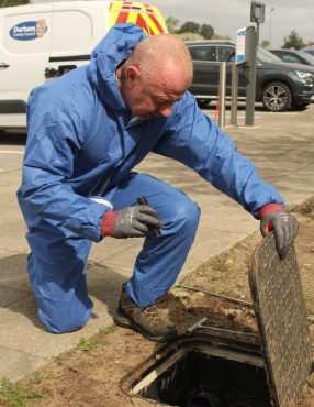 A man wearing a blue suit with the torch looking down a drain